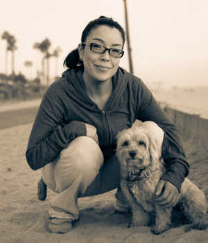 Nicole Narita crouching next to Linus the Maltipoo, at Dog Beach in Huntington Beach, California.